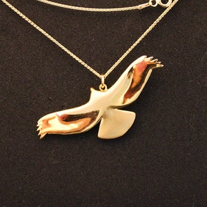 K&ouml;nnte beinhalten: Eine goldene Halskette mit einem Anh&auml;nger in Form eines Vogels im Flug. Der Vogel ist nach rechts gerichtet und hat seine Fl&uuml;gel ausgebreitet.