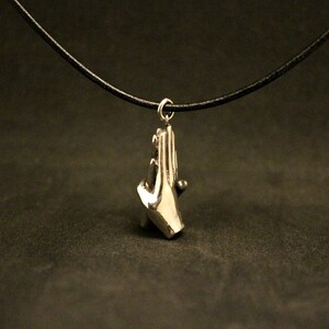 May include: A silver necklace with a pendant of two hands clasped together. The necklace is on a black cord.