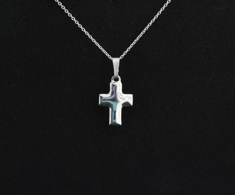 May include: A silver cross pendant necklace on a silver chain. The cross is simple and has a slightly raised design.