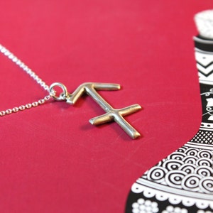 May include: A silver necklace with a Sagittarius zodiac sign pendant. The pendant is a simple, stylized design of the archer's arrow and bow.