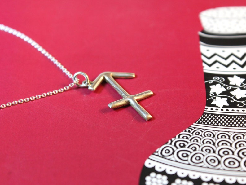 May include: A silver necklace with a Sagittarius zodiac sign pendant. The pendant is a simple, stylized design of the archer's arrow and bow.