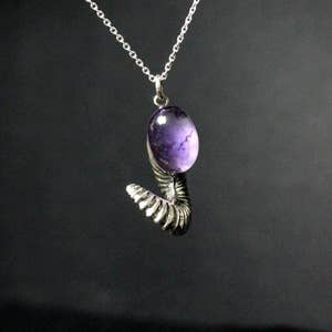 Pu&ograve; includere: Una collana d'argento con un ciondolo di ametista viola a forma di coda arrotolata.