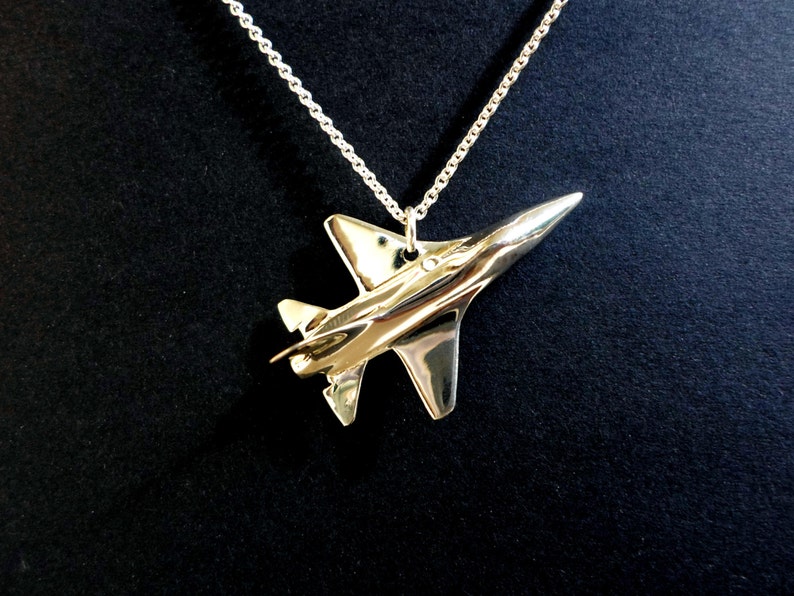 Op de afbeelding: Een zilveren ketting met een gedetailleerde hanger in de vorm van een straaljager.