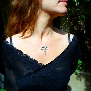 May include: A woman wearing a black lace top with a silver ram pendant necklace.