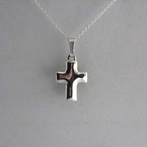 May include: A silver cross pendant necklace. The cross is simple and modern in design.