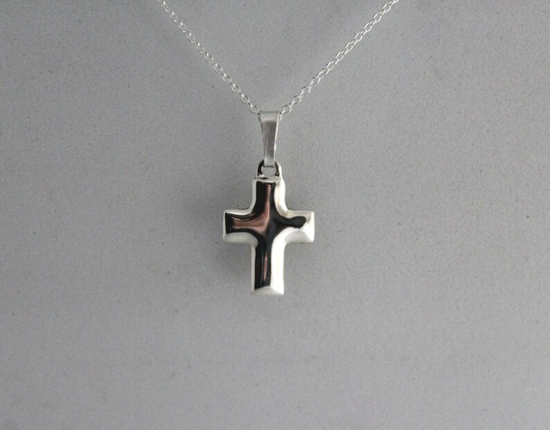 May include: A silver cross pendant necklace. The cross is simple and modern in design.