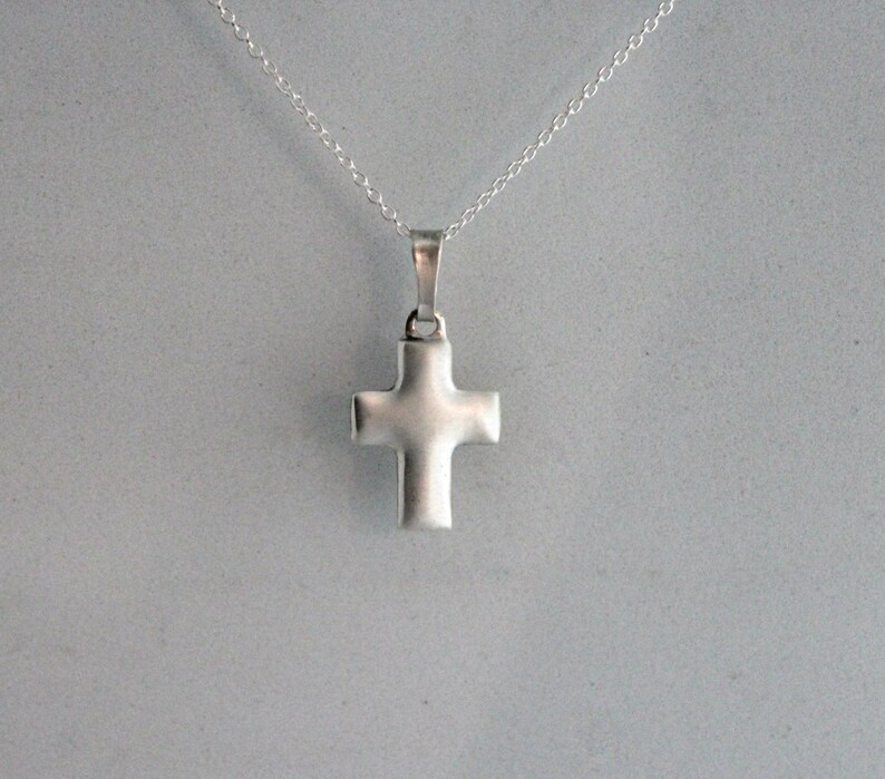 May include: A silver cross pendant on a silver chain necklace.