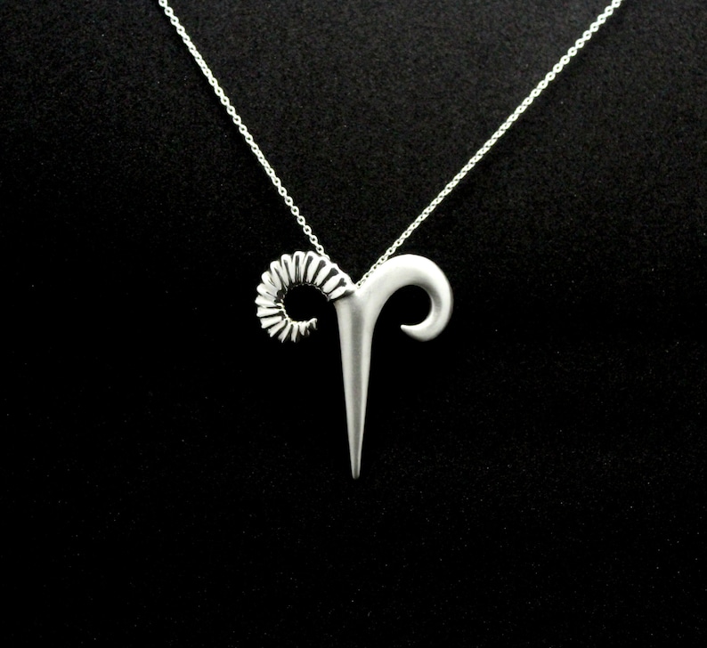 May include: Silver necklace with a ram's head pendant. The pendant is detailed with a curled horn and a pointed head.