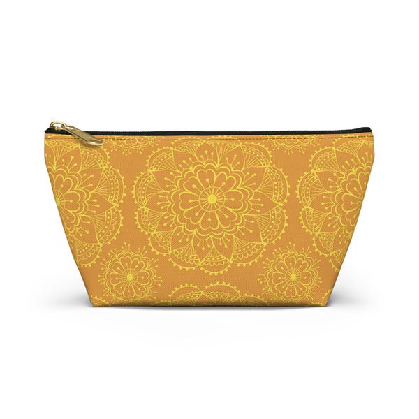 May include: A trapezoidal pouch with a gold zipper closure featuring a repeating yellow mandala pattern printed on a mustard orange background. The accessory has a black top edge and a structured base, displaying a symmetrical floral design.