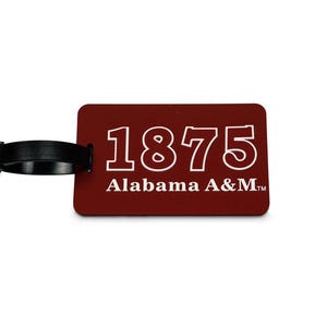 May include: A maroon luggage tag with the text "1875 Alabama A&M" in white. The tag has a black strap for attachment. The design is simple and the text is easy to read. The tag is rectangular with rounded corners.