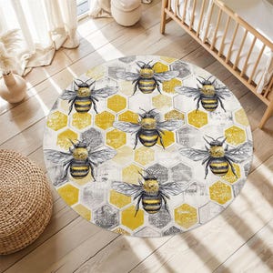 May include: A round rug featuring a honeycomb pattern in yellow and gray, with detailed illustrations of bees. The rug is placed on a wooden floor, creating a decorative accent for a room.