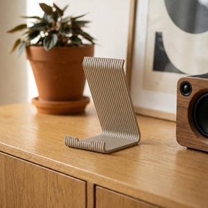 Peut inclure: Un support de téléphone beige présentant une surface texturée et nervurée avec un design en forme de L incurvé. Le support possède une base plate et un dossier incliné, composé d'une série de stries verticales parallèles sur toute la longueur.
