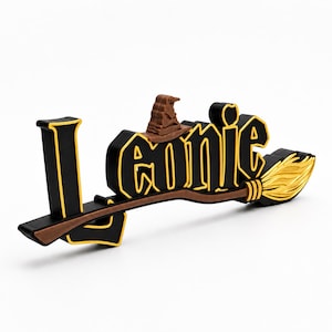 Könnte beinhalten: Ein dreidimensionales Schild mit dem Namen Leonie in schwarzen Buchstaben mit gelben Umrandungen. Ein brauner Zauberhut sitzt auf dem Buchstaben o und ein brauner Besen mit gelben Borsten erstreckt sich horizontal über die Basis der Schrift.