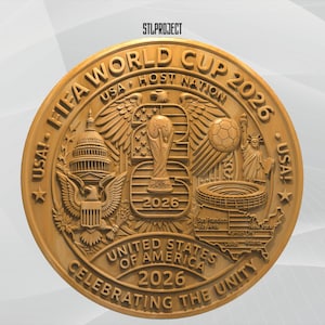 May include: A circular gold-toned commemorative medallion featuring the text FIFA WORLD CUP 2026, USA HOST NATION, UNITED STATES OF AMERICA, and CELEBRATING THE UNITY. The design includes the US Capitol, an eagle, a soccer ball, and a map of the USA.