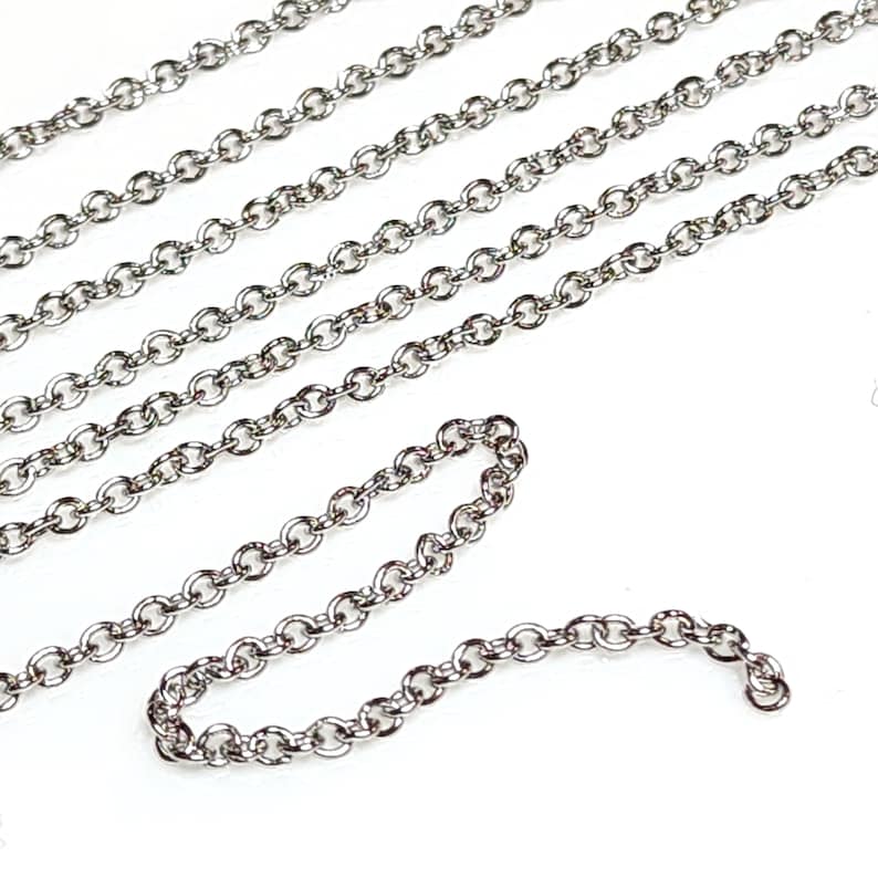 Puede incluir: Una cadena de plata con un delicado dise&ntilde;o de eslabones redondos. La cadena est&aacute; dispuesta en un patr&oacute;n suelto y fluido sobre un fondo blanco.