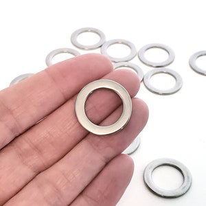 May include: A close-up of a silver jump ring, a type of metal ring used in jewelry making. The jump ring is held in a hand, and there are several other jump rings in the background.