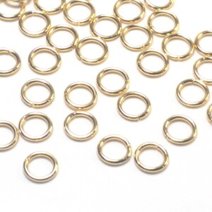 K&ouml;nnte beinhalten: Eine Ansammlung kleiner, kreisf&ouml;rmiger goldfarbener Metall-Biegeringe, die &uuml;ber den Rahmen verstreut sind. Jeder einzelne Ring hat eine glatte, polierte Oberfl&auml;che und eine sichtbare Nahtstelle, an der die Drahtenden aufeinandertreffen.
