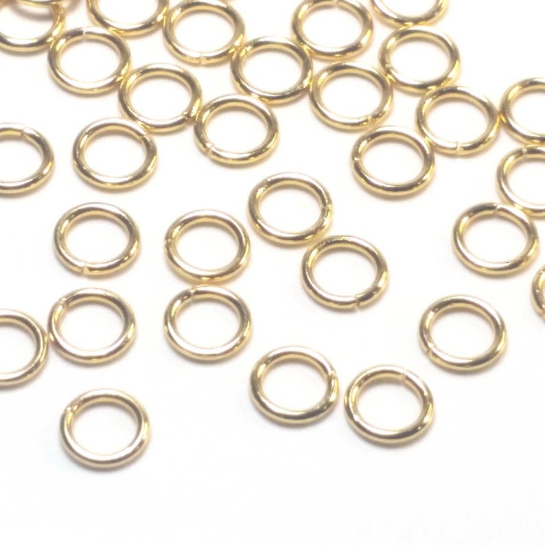 K&ouml;nnte beinhalten: Eine Ansammlung kleiner, kreisf&ouml;rmiger goldfarbener Metall-Biegeringe, die &uuml;ber den Rahmen verstreut sind. Jeder einzelne Ring hat eine glatte, polierte Oberfl&auml;che und eine sichtbare Nahtstelle, an der die Drahtenden aufeinandertreffen.