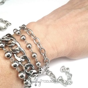 May include: A silver chain bracelet with a chunky link design, layered with a beaded chain and two smaller chain bracelets.