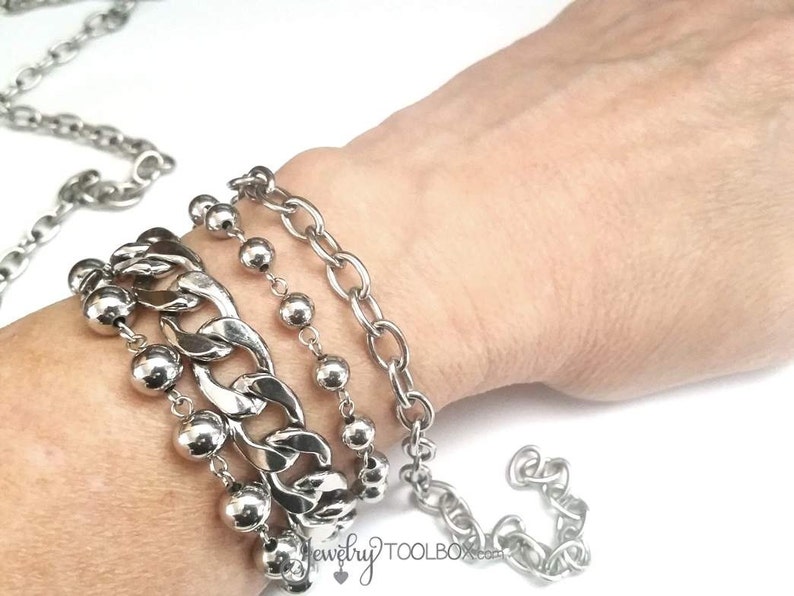 May include: A silver chain bracelet with a chunky link design, layered with a beaded chain and two smaller chain bracelets.
