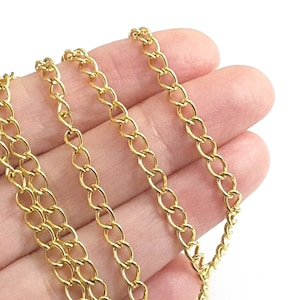 May include: Close-up of a gold-colored chain with oval links. The chain is held in a hand against a white background. The chain is made of small, evenly spaced links.