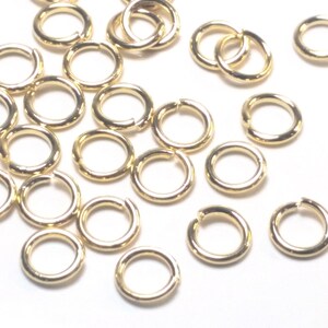 K&ouml;nnte beinhalten: Eine Ansammlung kleiner, kreisf&ouml;rmiger goldfarbener Metall-Biegeringe, die &uuml;ber den Rahmen verstreut sind. Jeder einzelne Ring weist einen einzelnen offenen Schnitt entlang seines Umfangs auf, der zum Verbinden von Schmuckkomponenten oder anderen kleinen Bastelartikeln dient.