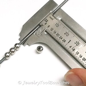 May include: A close-up of a metal ruler measuring a silver bead. The ruler is marked in millimeters and inches. The bead is about 4 millimeters in diameter.