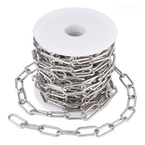 May include: A roll of silver chain link, with a portion of the chain uncoiled. The chain is made of metal and has a shiny finish.