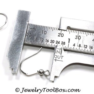 May include: A close-up of a silver earring hook measured with a ruler. The hook is 28 mm long.