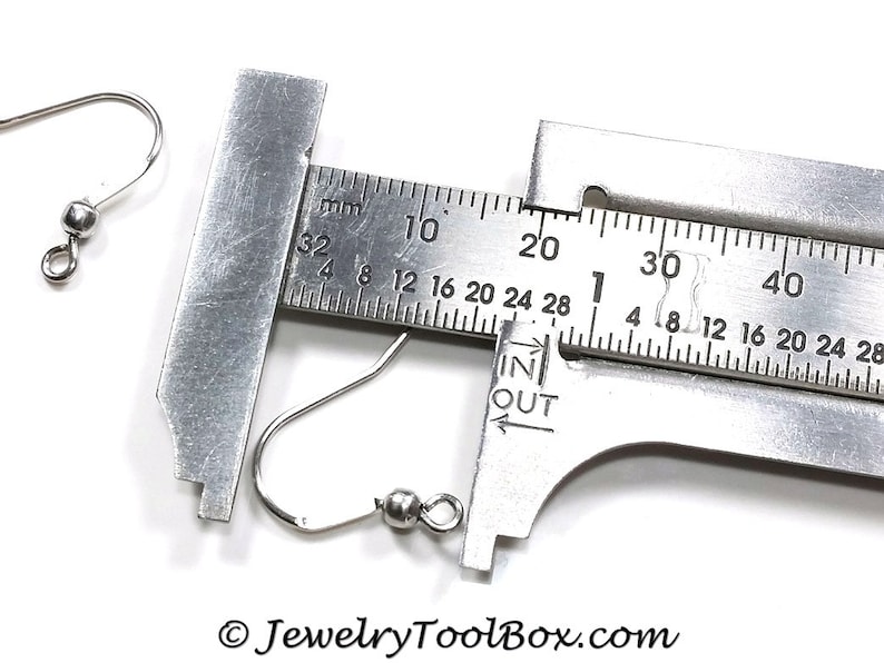 May include: A close-up of a silver earring hook measured with a ruler. The hook is 28 mm long.