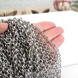 May include: A close-up of a silver chain, showing the individual links. The chain is lying on a white surface.