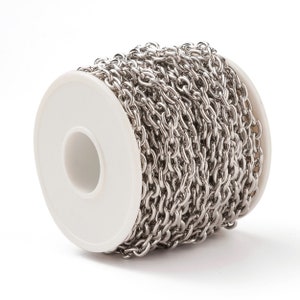 May include: A roll of silver chain, wound around a white spool. The chain is made of small, linked metal pieces.