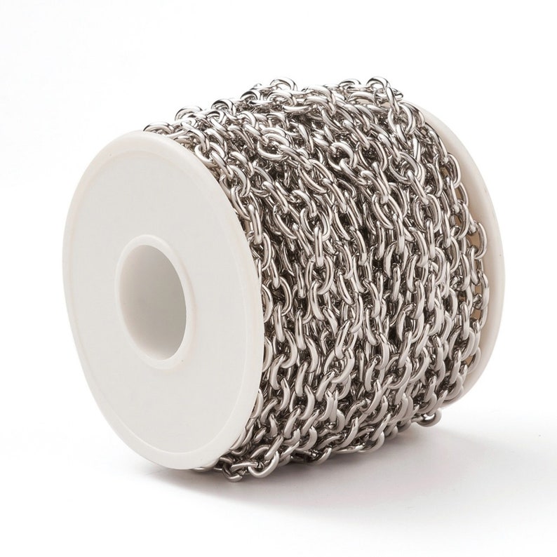 May include: A roll of silver chain, wound around a white spool. The chain is made of small, linked metal pieces.