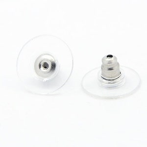 May include: Two clear plastic earring backs with silver metal posts. The backs are round and have a small hole in the center. The posts are cylindrical and have a rounded top.
