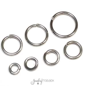 May include: An assortment of silver-colored jump rings in various sizes, arranged on a white surface. The jump rings are open, ready for use in jewelry making or other crafts. The image includes the text "Jewelry TOOLBOX".
