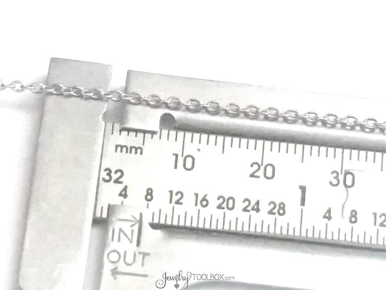 May include: A close-up of a silver chain measured with a ruler. The ruler shows measurements in millimeters from 32 to 30. The chain is 1 mm wide.