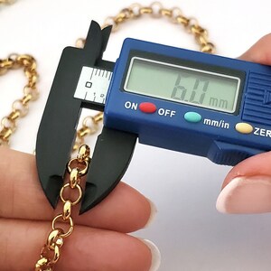 May include: Close-up of a gold chain being measured with a digital caliper. The caliper reads 6.0 mm.