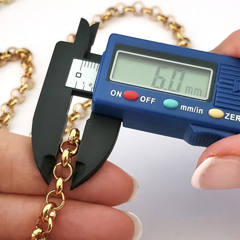 May include: Close-up of a gold chain being measured with a digital caliper. The caliper reads 6.0 mm.