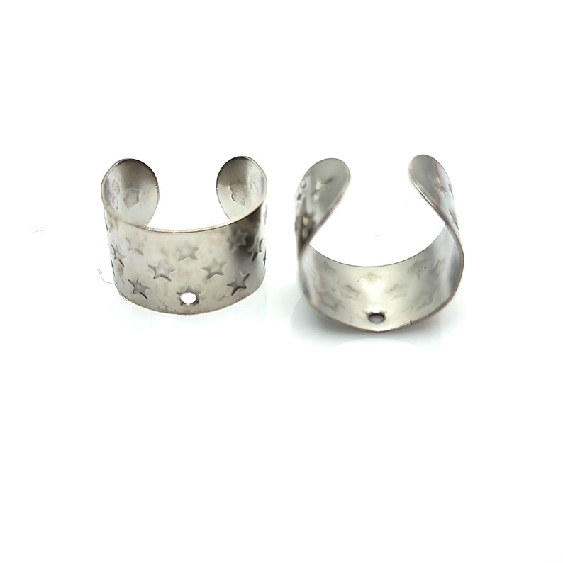 May include: Two silver metal rings with a star pattern. The rings are open and have a small hole in the center.
