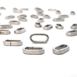 May include: A close-up of a group of silver oval jump rings. The rings are scattered on a white surface. The rings are about 1/2 inch in diameter.