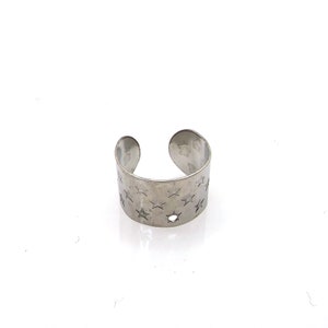May include: A silver ear cuff with a star pattern. The cuff is open on one side and has a small hole in the center.