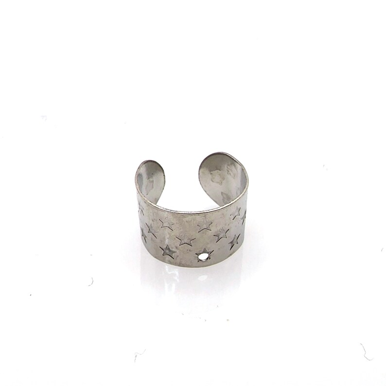 May include: A silver ear cuff with a star pattern. The cuff is open on one side and has a small hole in the center.