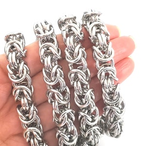 May include: Four silver chain bracelets, each with a unique interlocking pattern, are displayed on a hand. The bracelets are made of metal and have a shiny finish.