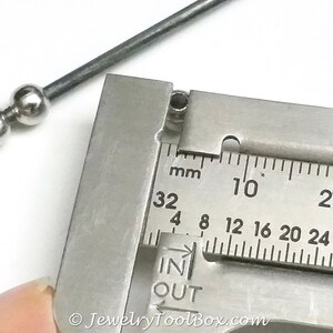 May include: Close-up of a silver metal bead measured with a caliper. The caliper reads 32 mm, 4 mm, 8 mm, 12 mm, 16 mm, 20 mm, 24 mm, 28 mm, 10, 20, and 1. The caliper has the words "IN" and "OUT" printed on it.
