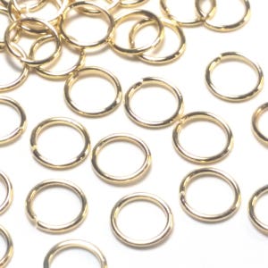K&ouml;nnte beinhalten: Eine Ansammlung zahlreicher kleiner, kreisf&ouml;rmiger goldfarbener Metall-Biegeringe, die &uuml;ber den Rahmen verstreut sind. Jeder einzelne Ring besteht aus einem d&uuml;nnen Draht mit einem sichtbaren Schlitz, der f&uuml;r Schmuckarbeiten gedacht ist.
