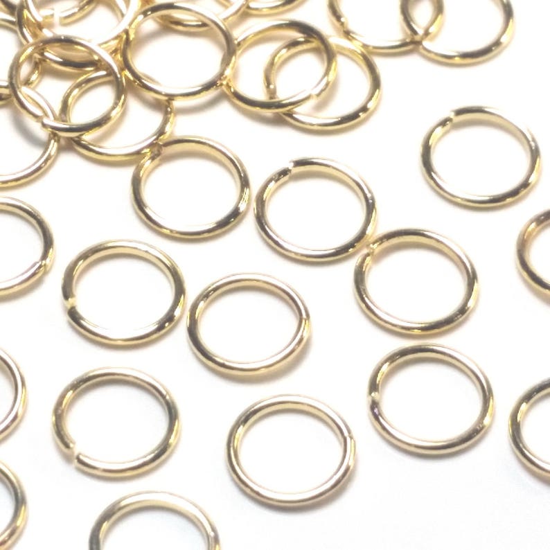 K&ouml;nnte beinhalten: Eine Ansammlung zahlreicher kleiner, kreisf&ouml;rmiger goldfarbener Metall-Biegeringe, die &uuml;ber den Rahmen verstreut sind. Jeder einzelne Ring besteht aus einem d&uuml;nnen Draht mit einem sichtbaren Schlitz, der f&uuml;r Schmuckarbeiten gedacht ist.