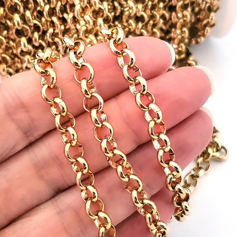 May include: Three strands of gold chain link, each with a different length, are held in a hand. The chain links are round and have a polished finish.