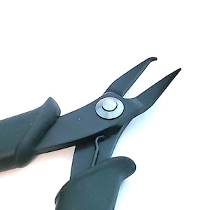 May include: Black pliers with black rubber handles and a silver metal rivet. The pliers have a pointed tip and are designed for jewelry making.