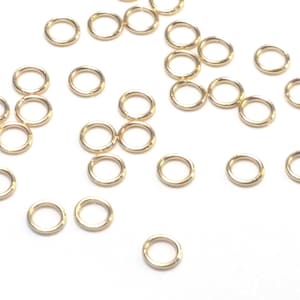 K&ouml;nnte beinhalten: Eine Ansammlung kleiner, kreisf&ouml;rmiger goldfarbener Metall-Biegeringe, die &uuml;ber das Bild verstreut sind. Jeder einzelne Ring besteht aus einem d&uuml;nnen, glatten Draht mit einer sichtbaren Nahtstelle, an der die Enden aufeinandertreffen.