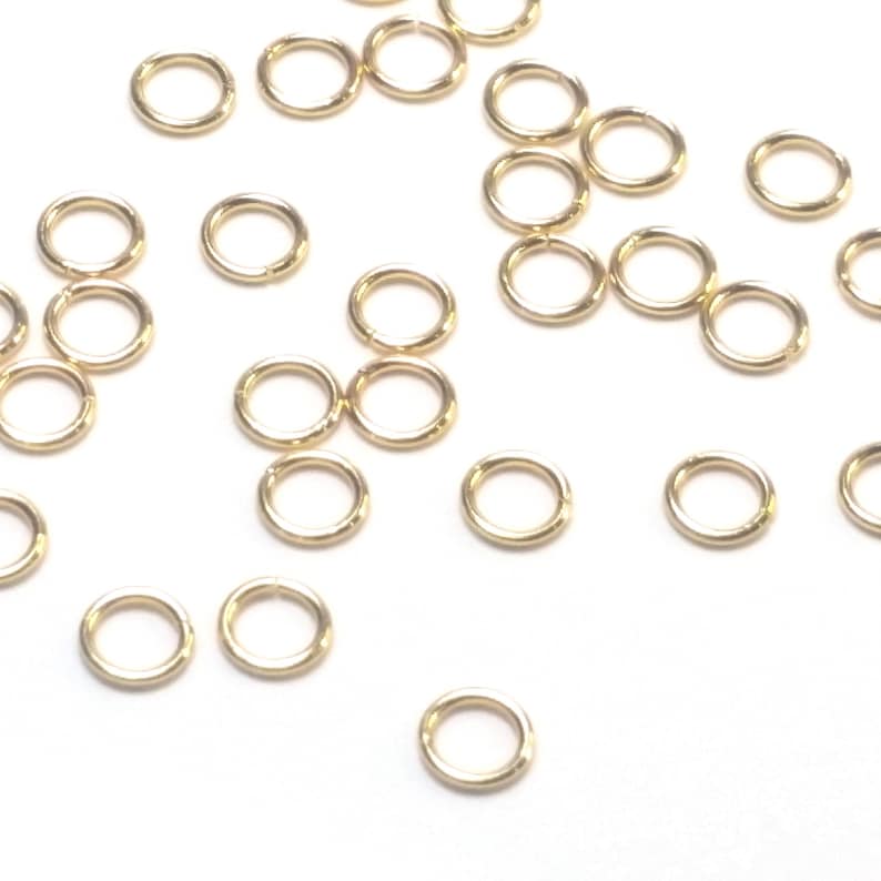 K&ouml;nnte beinhalten: Eine Ansammlung kleiner, kreisf&ouml;rmiger goldfarbener Metall-Biegeringe, die &uuml;ber das Bild verstreut sind. Jeder einzelne Ring besteht aus einem d&uuml;nnen, glatten Draht mit einer sichtbaren Nahtstelle, an der die Enden aufeinandertreffen.